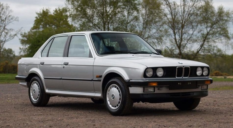 BMW série 3 E30 4 portes grise avec enjoliveurs, version d'entrée de gamme