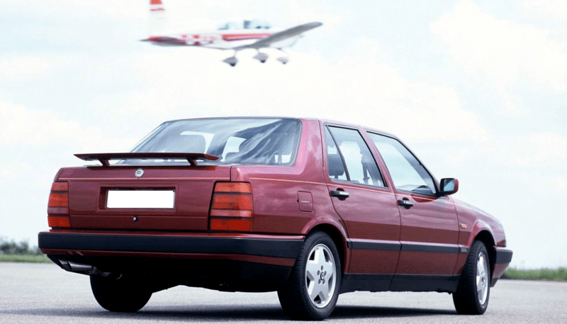 Lancia Thema rouge bordeaux vue de l'arrière avec aileron arrière déployé.