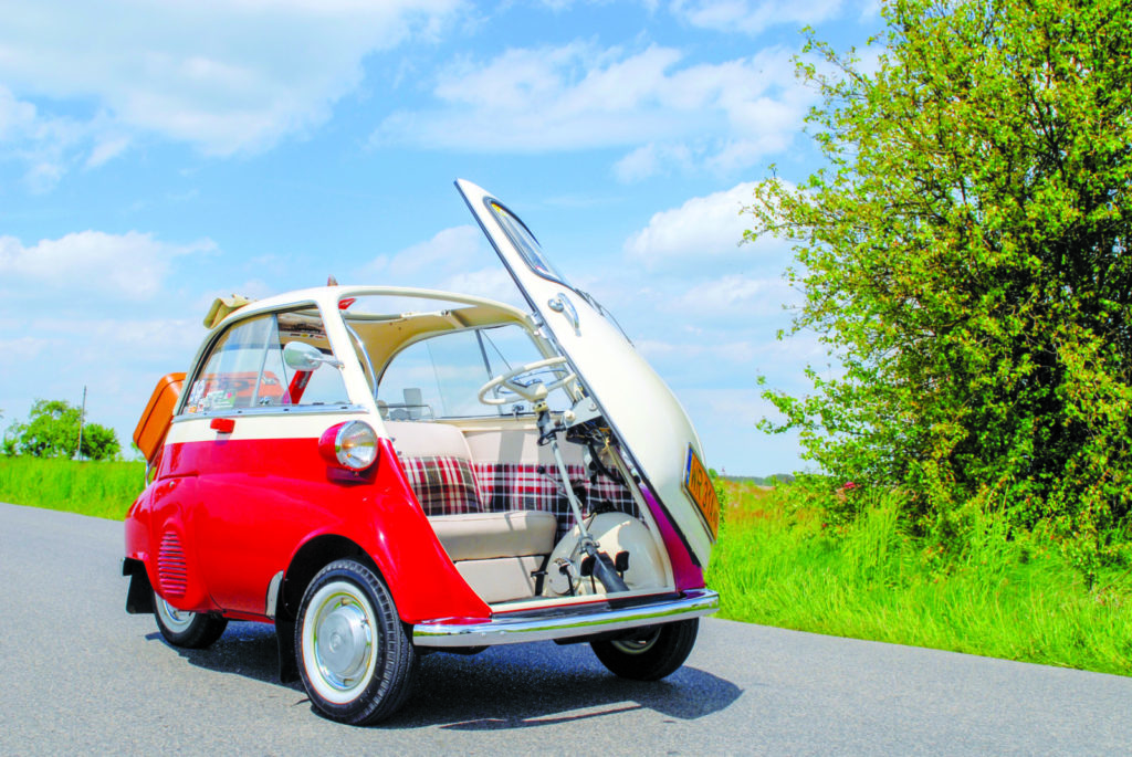 BMW Isetta 250 rouge et blanche garée sur bord de route avec porte ouverte.