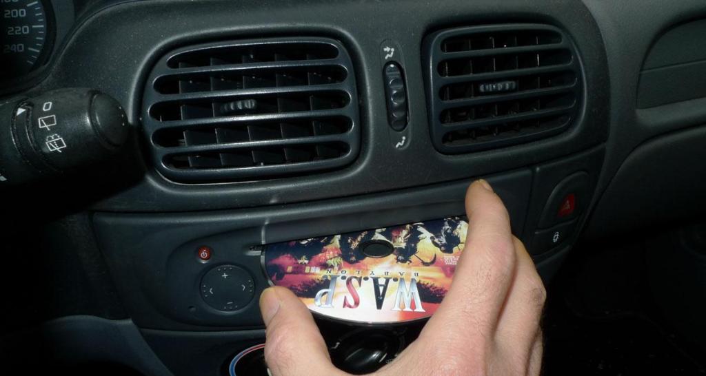 Console centrale d'une Renault Mégane 1ère génération intégrant un autoradio CD avec main qui insert un CD à l'intérieur.