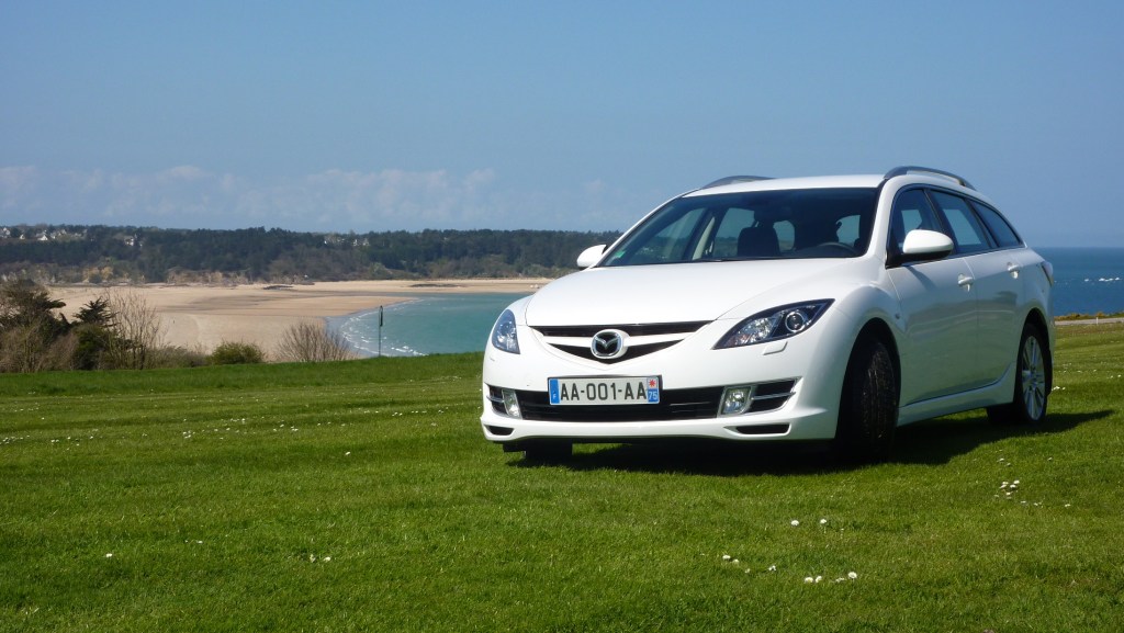 Mazda 6 break blanche devant plage avec immatriculation AA-001-AA.