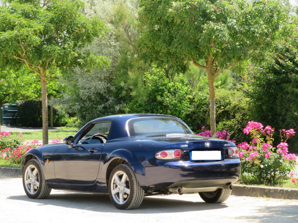 Mazda MX-5 NC bleue coupé garée devant des fleurs.