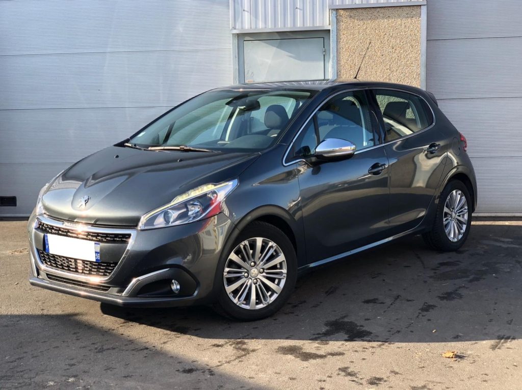 Peugeot 208 II de couleur grise garée devant bâtiment.