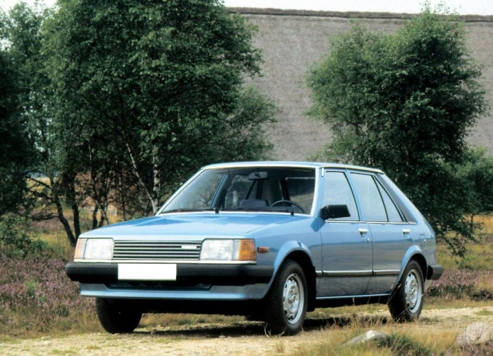 Mazda 323 BD bleue sur chemin de campagne.