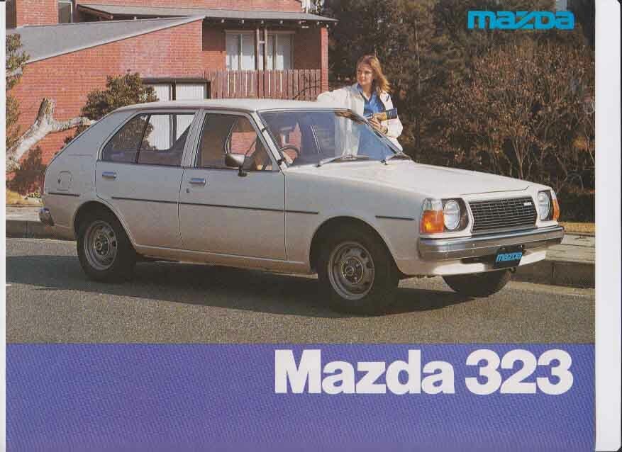Photo publicitaire de la Mazda 323 FA blanche dans la rue avec jeune femme à côté.