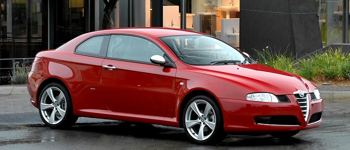 Alfa Roméo GT 3.2 V6 Busso rouge garée devant bureau.